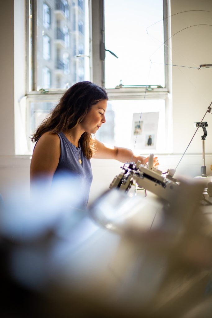 Carolyn Ferreira working at a knitting machine in her studio in Victoria BC